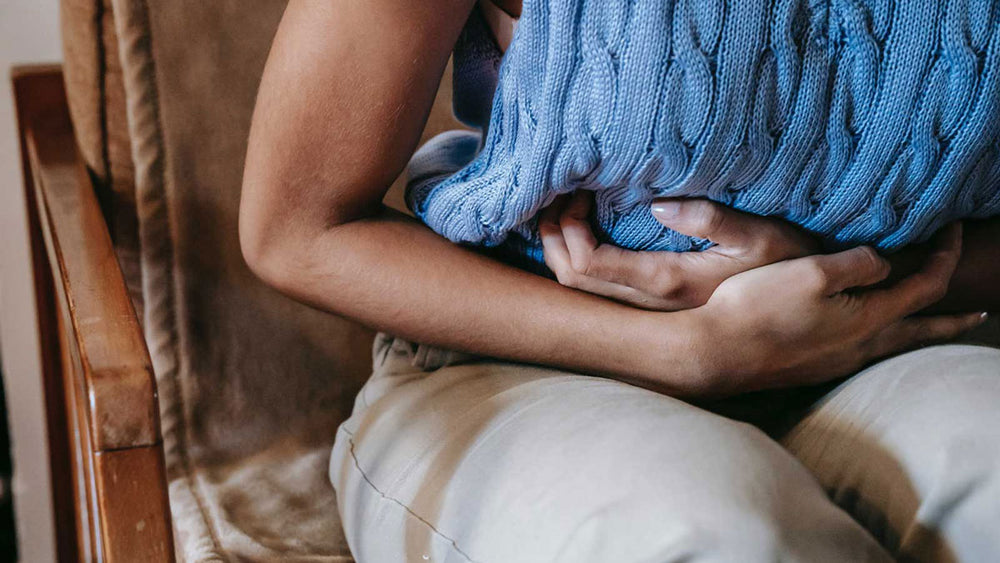 Person sitting on a chair clutching their stomach because of heartburn pain